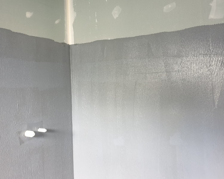 Waterproofing application in progress on bathroom walls with grey sealant.