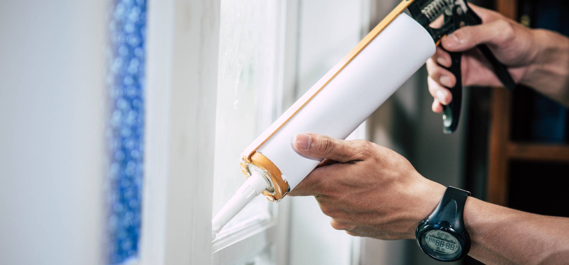 Close-up of a professional’s hands applying sealant from a caulking gun to a window joint, ensuring airtight insulation