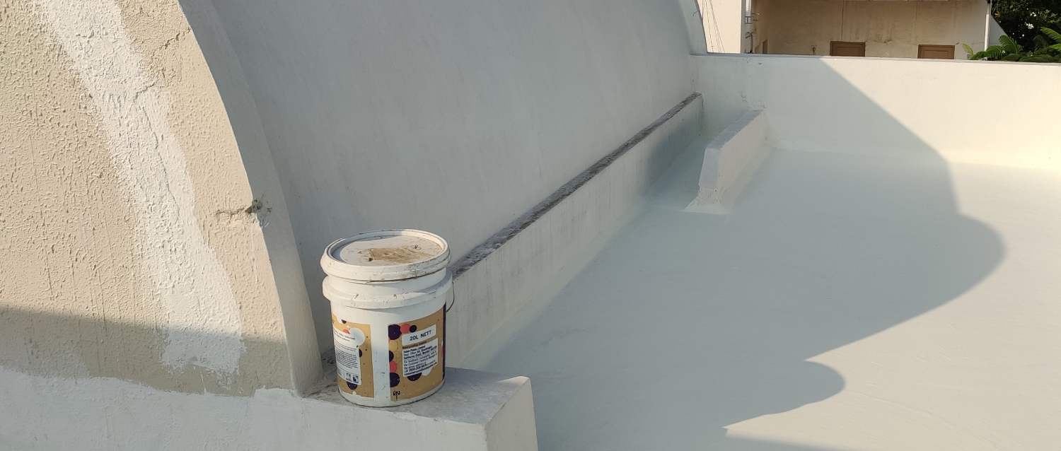 A freshly waterproofed roof with a white reflective coating and an open bucket of waterproof sealant.