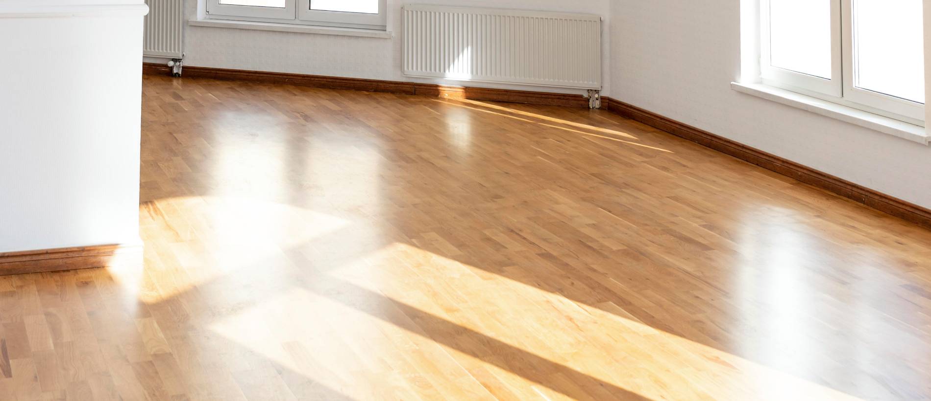 A well-lit room with sunlight casting on a professionally sealed wooden floor, showcasing the glossy finish and the quality of work.